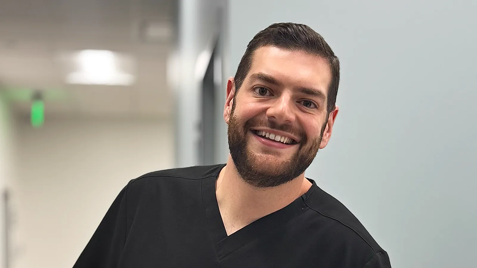 Dr. Joshua Brady smiling in black scrubs in the hallway at Tampa Bay Dermatology
